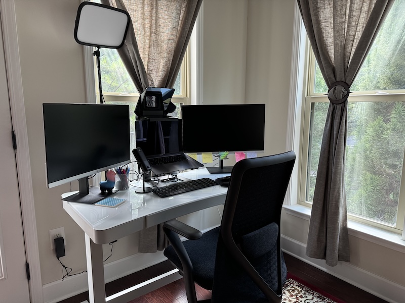 Photo of upgraded work from home setup: adjustable desk, dual monitors, external microphone, key light, prompters