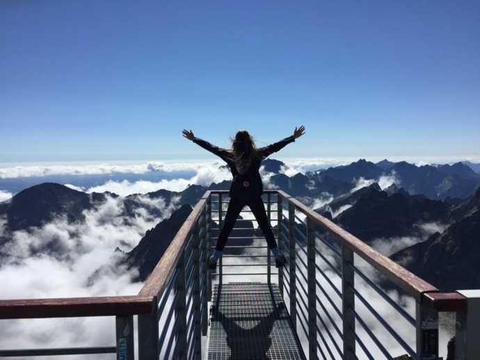 woman jumping for joy overlooking a valley of mountain ranges before her