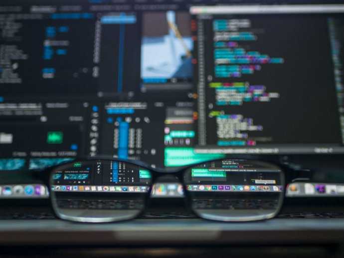 pair of glasses resting on a desk in front of screens filled with code