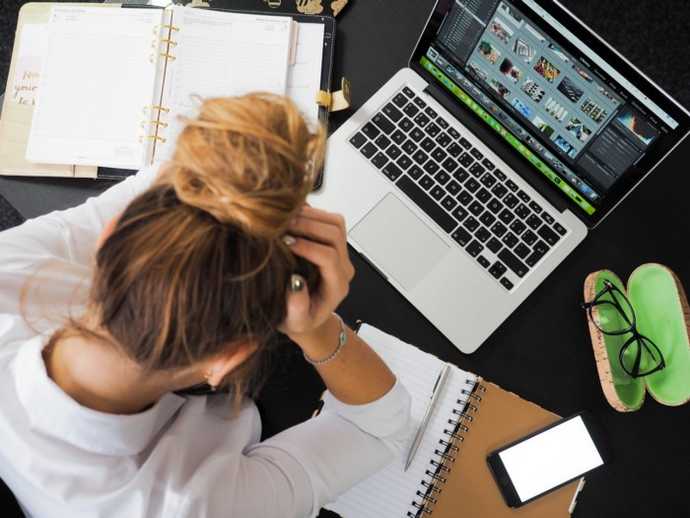 a woman looking defeated in front of her laptop, head in hands